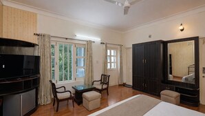 A bedroom with a bed, a TV, a wardrobe, a chair, a table, and a ceiling fan. - DLS Tehri Club Resort (Tehri)