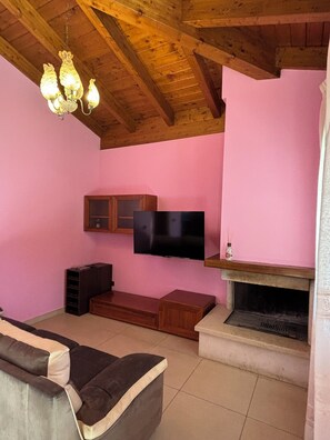 A living room with a wooden ceiling, a flat-screen TV mounted on the wall, a fireplace, and a sofa.