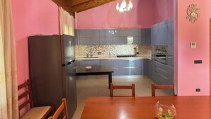 A dining area with a wooden table and chairs, a chandelier, and a kitchen in the background. - VILLA PAOLA L'AQUILA (Abruzzo)