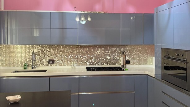 A modern kitchen with grey cabinets, a pink wall, and a chandelier. - VILLA PAOLA L'AQUILA (Abruzzo)
