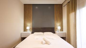 Una habitación de hotel con una cama grande, dos mesitas de noche, un cabecero y una ventana con cortinas.