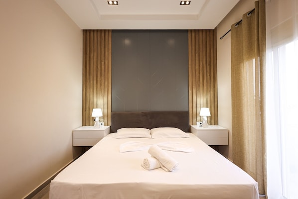 A hotel room with a large bed, two bedside tables, a headboard, and a window with curtains. - AZZURRA Studios (Durrës)