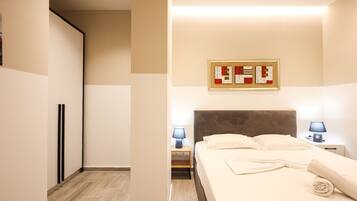 Quarto de hotel com cama, abajures, cabeceira, uma obra de arte na parede e piso de madeira.