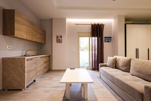 A modern kitchen with wooden cabinets and a white countertop, a beige sofa, and a dining table in a bright living area. - AZZURRA Studios (Durrës)