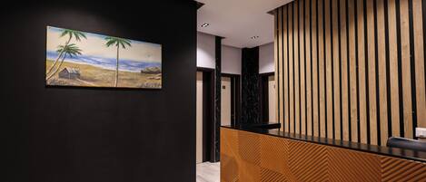 A reception area with a wooden panel design, a painting of a beach scene, and a reception desk.