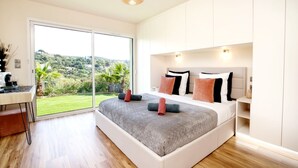 A modern bedroom with a large bed, a desk, and a view of a green landscape through a sliding door. - Villa Les Oiseaux Du Paradis Cavalaire-sur-mer (Cavalaire-sur-Mer)