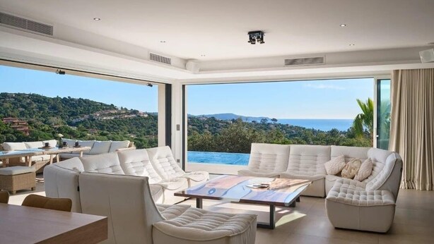 A spacious living room with a large window offering a scenic view of a hillside and ocean. - Villa Les Oiseaux Du Paradis Cavalaire-sur-mer (Cavalaire-sur-Mer)