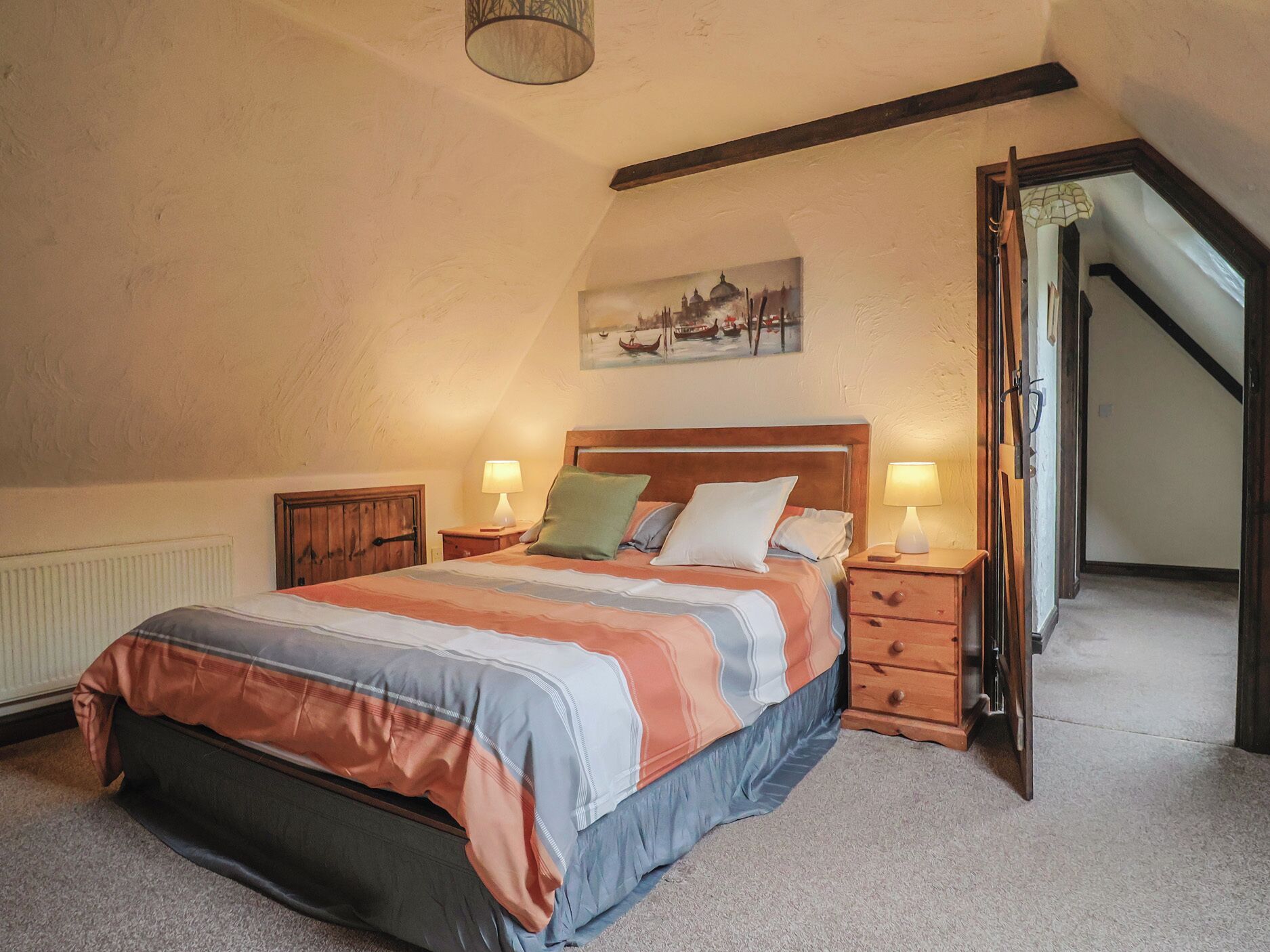 A bedroom with a bed, two bedside tables, a painting on the wall, and a staircase leading to an upper level.