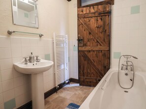 Un bany amb un lavabo blanc, una banyera, una porta de fusta i un mirall a la paret.