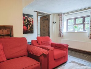 A room with a red sofa, a wooden door, a window with curtains, and a painting on the wall. - Cider Cottage - Near Lyme Regis (Axminster)