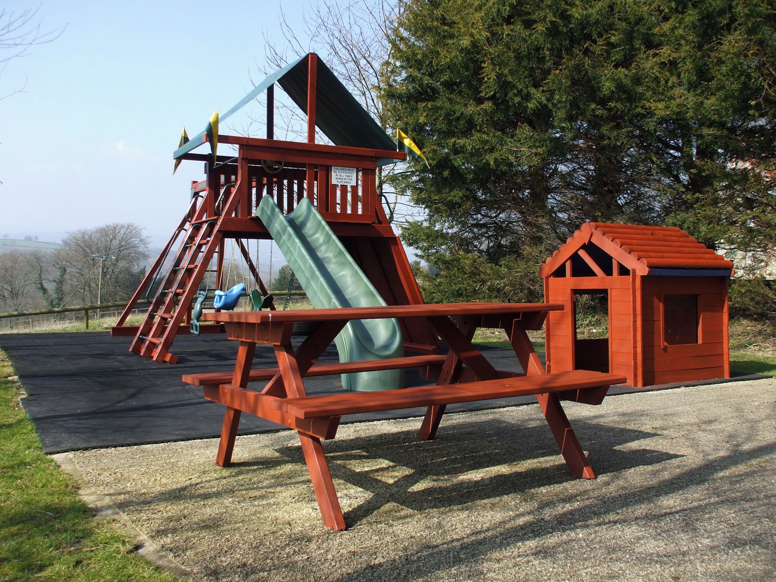 A playground with a slide, swings, and a small red playhouse.