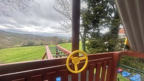 A wooden deck with a yellow steering wheel, green railings, and a view of a green field and trees. - Cider Cottage - Near Lyme Regis (Axminster)