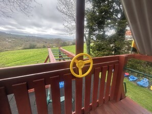 A wooden deck with a yellow steering wheel, green railings, and a view of a green field and trees. - Cider Cottage - Near Lyme Regis (Axminster)
