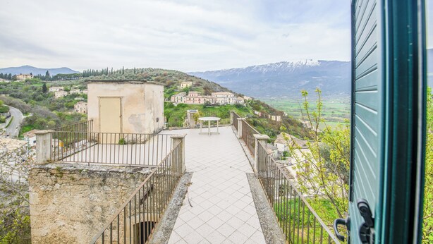 A terrace with a view of a hillside village, a table, and a door. - Casa Phoebe (Capestrano)