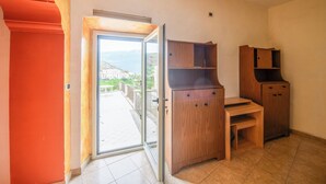 A room with a sliding glass door leading to a balcony, wooden furniture, and a tiled floor. - Casa Phoebe (Capestrano)