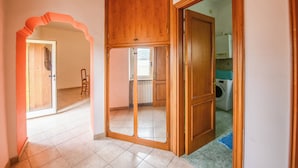 An interior with a wooden door, a tiled floor, and a glimpse of a kitchen area. - Casa Phoebe (Capestrano)