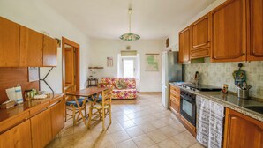 A kitchen with wooden cabinets, a dining table with chairs, a refrigerator, and a stove. - Casa Phoebe (Capestrano)