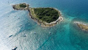 Vista aérea de uma área costeira com águas turquesa cristalinas, afloramentos rochosos e uma pequena ilha com vegetação densa.