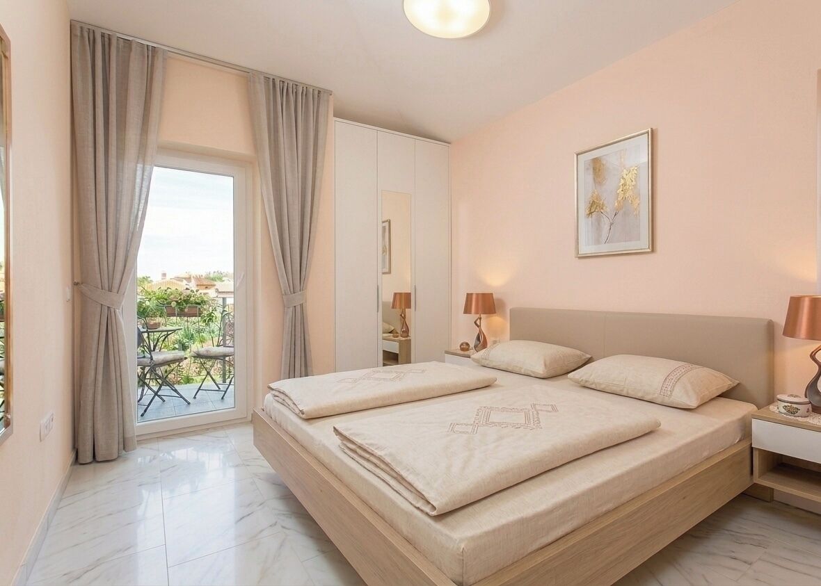 Habitación de hotel con cama, mesitas de noche, ventana con cortinas, balcón y un cuadro en la pared.