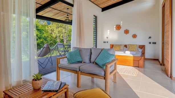 Una sala moderna con un sofá, un comedor y vistas al verde exterior.