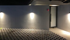 Fachada moderna de un edificio con piso estampado, una puerta y una señal de salida de emergencia roja, y dos luces fijadas a la pared.