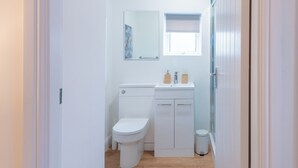 A compact bathroom with a toilet, sink, and mirror. - Glan Neigr by Guestz (Rhosneigr)