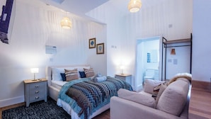 A bedroom with a bed, bedside tables, a chair, a wardrobe, and a hanging light fixture. - Glan Neigr by Guestz (Rhosneigr)
