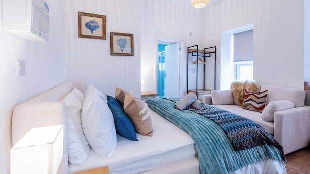 A modern, well-lit room with a bed, a sofa, and a hanging light fixture. - Glan Neigr by Guestz (Rhosneigr)
