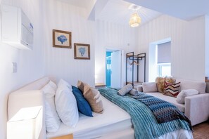 A modern, well-lit room with a bed, a sofa, and a hanging light fixture.