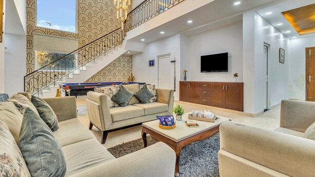 A spacious living area with a sofa, coffee table, and a staircase leading to an upper level. - Alaya Stays Ratikara Ullaas 2BHK Pool (Ballabgarh)