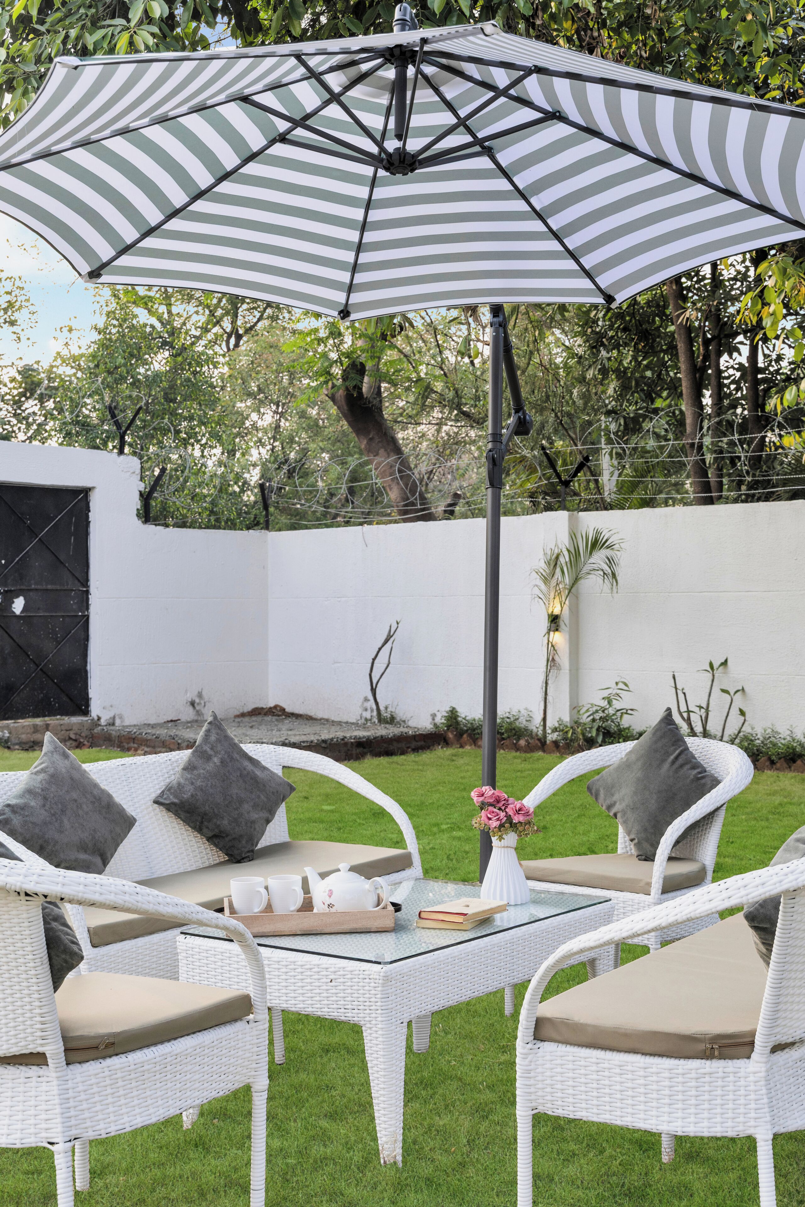 Un patio con muebles de mimbre, una sombrilla a rayas y una pared blanca al fondo.