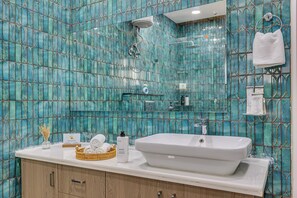 A bathroom with a large white sink, a mirror, and a shower. There are towels and toiletries on the counter. - Alaya Stays Ratikara Ullaas 2BHK Pool (Ballabgarh)