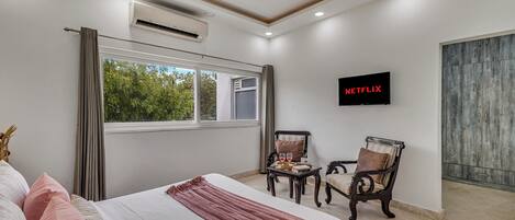 A hotel room with a bed, a TV, a window, and a view of greenery outside.