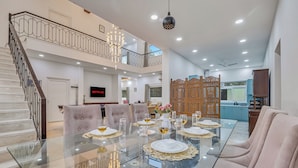 A spacious living area with a glass dining table set for six, a staircase, a TV, and a decorative wooden partition. - Alaya Stays Ratikara Ullaas 2BHK Pool (Ballabgarh)