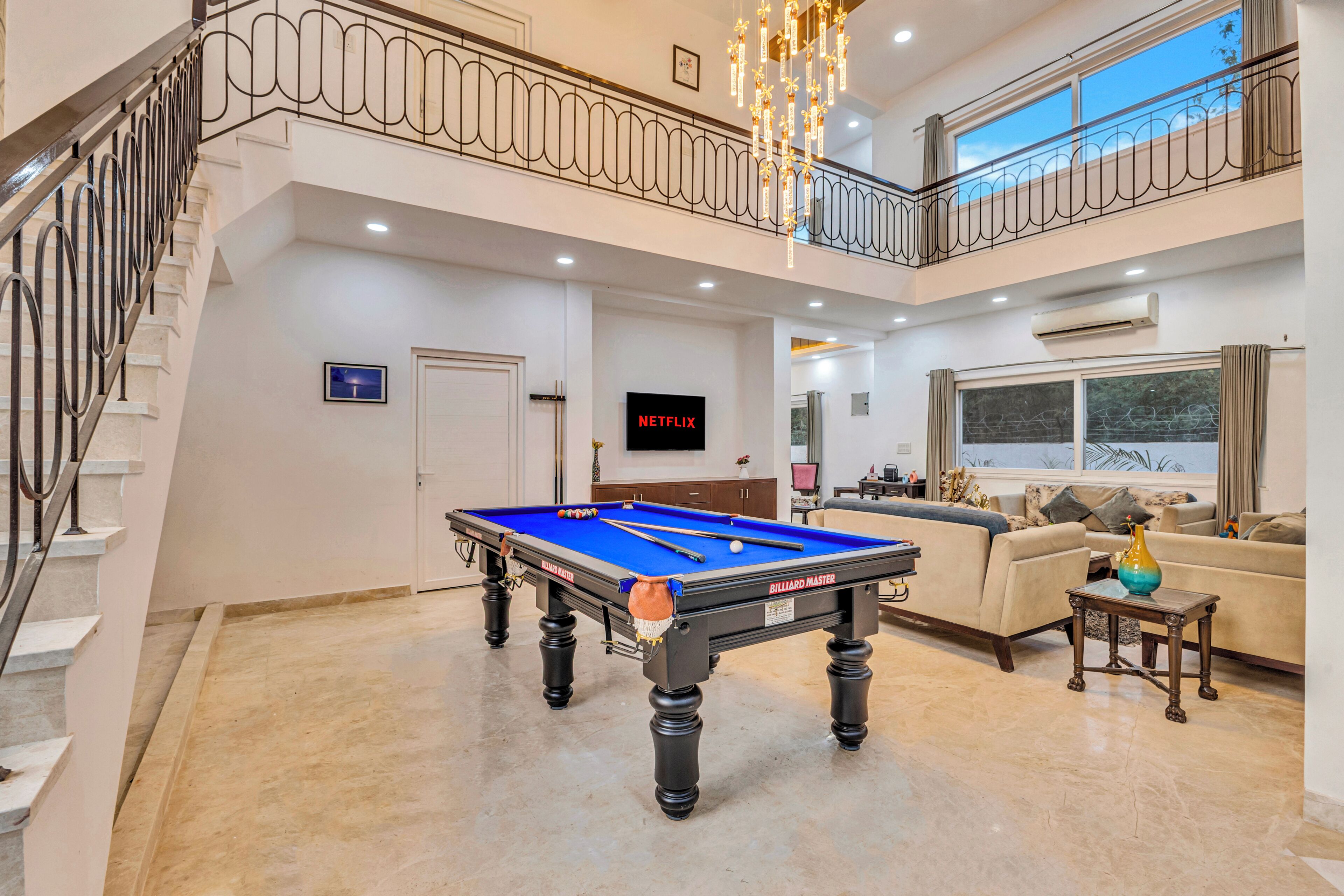 Un vaste espace de vie comprenant une table de billard, un escalier et un balcon.