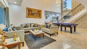 A spacious living area with a pool table, sofas, and a painting on the wall. - Alaya Stays Ratikara Ullaas 2BHK Pool (Ballabgarh)