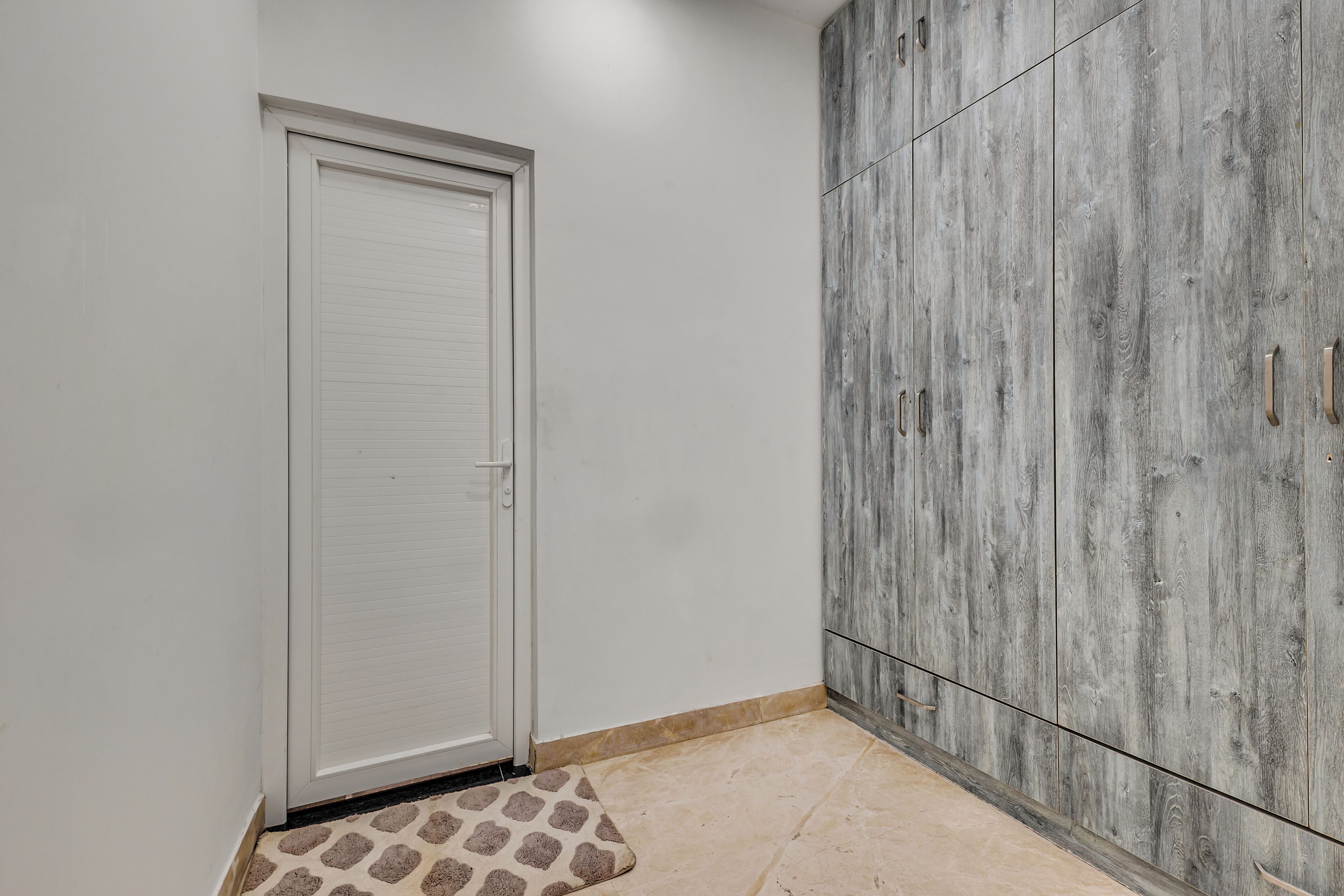 A room with a white door, a grey wardrobe, and a patterned rug.
