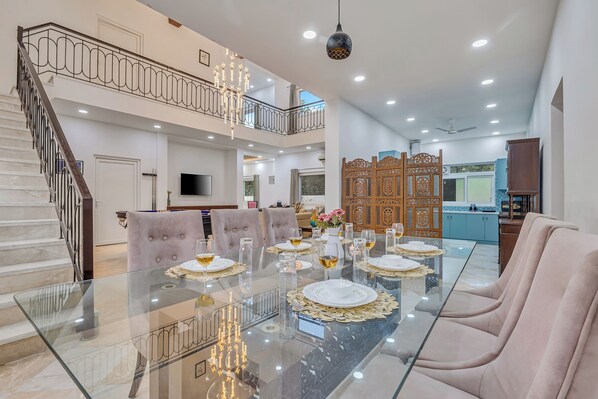A spacious dining area with a glass table, cushioned chairs, and a staircase leading to an upper level.