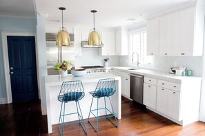 Uma cozinha moderna com armários brancos, uma ilha central com banquetas e iluminação pendente.