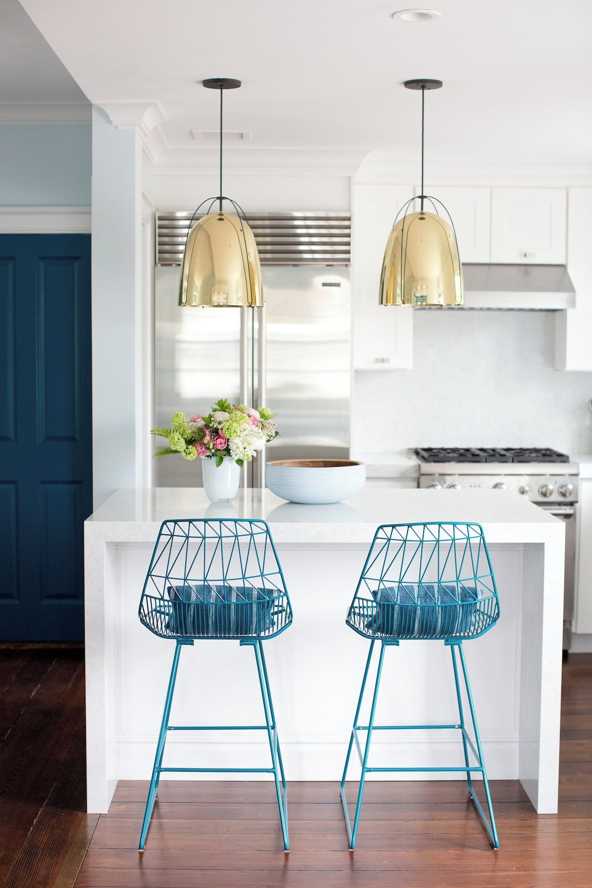 A modern kitchen with two blue wire chairs, a white island, and pendant lights.