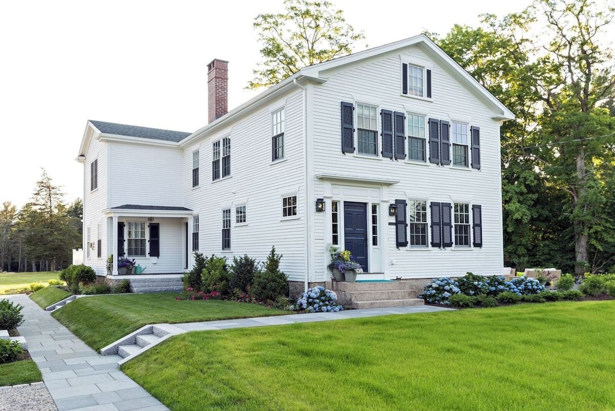 A two-story white house with a front porch, a chimney, and a well-maintained lawn.