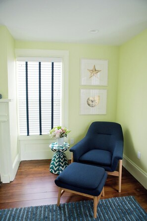 A room with a blue armchair, a small table with a vase of flowers, and a window with blinds. - New Marion renovated, bright, cozy home! (Marion)