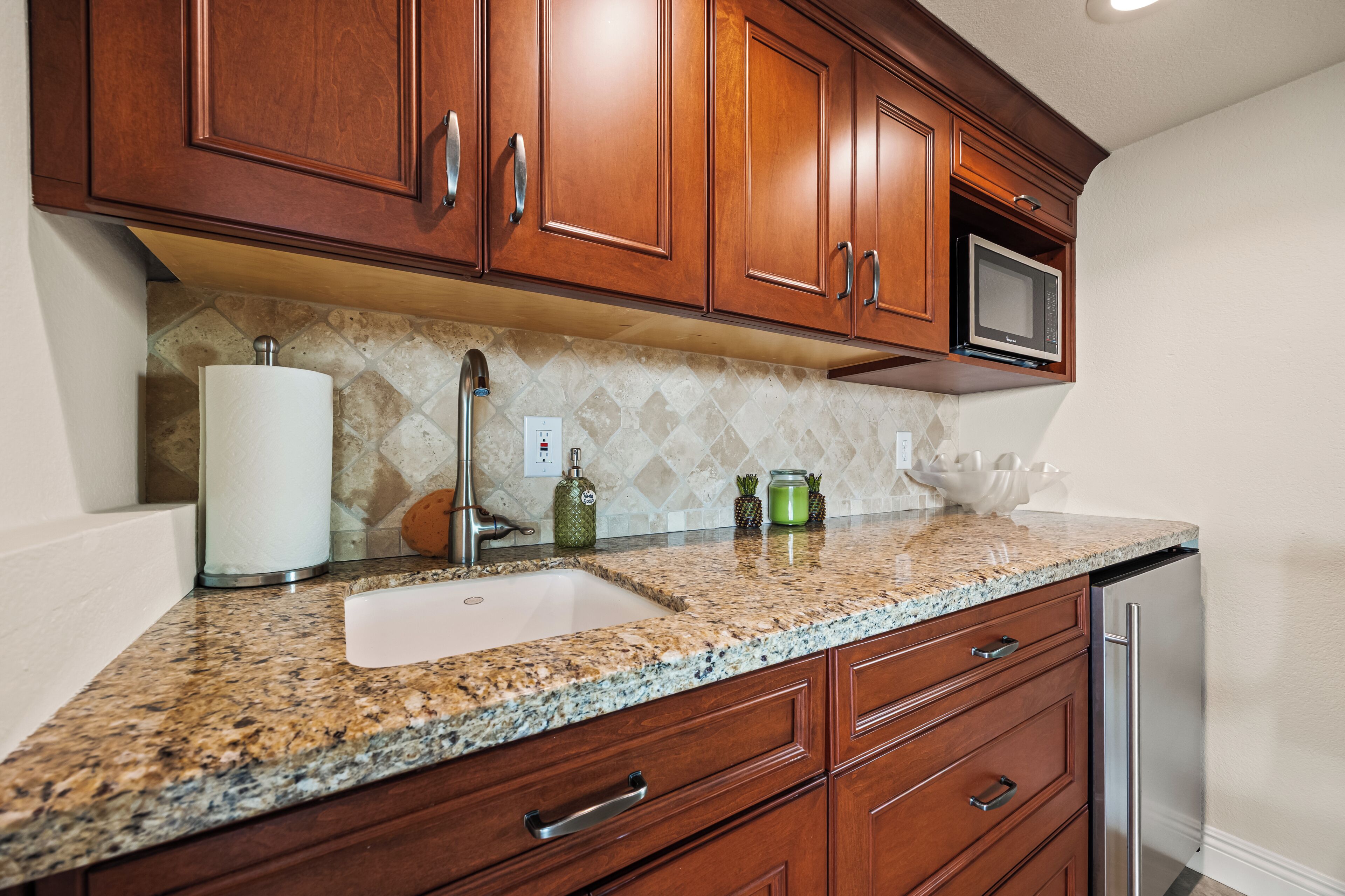 A kitchen with wooden cabinets, a granite countertop, a stainless steel sink, and a microwave.