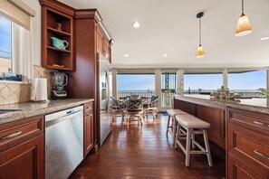 A kitchen with wooden cabinets, stainless steel appliances, a dining area with chairs, and a view to the outside.