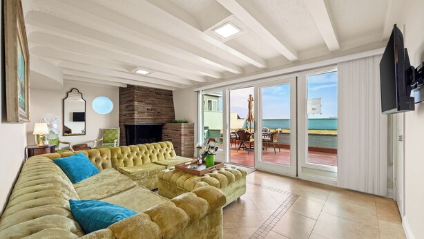 Uma sala de estar ampla com um sofá seccional grande, uma lareira e vista para o mar através de grandes portas deslizantes.