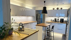 A modern kitchen with white cabinets, a wooden countertop, a kettle, a hanging light, and a coffee maker. - Villa Bee Mehiläinen (Vantaa)