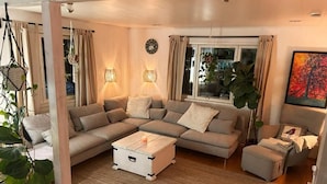A modern living room with a sectional sofa, a coffee table, and a small ottoman. There are two wall-mounted lamps and a large window with curtains. - Villa Bee Mehiläinen (Vantaa)