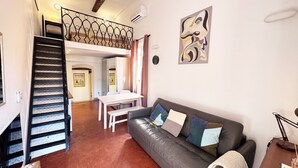 Ein Wohnzimmer mit Sofa, Tisch, Treppe und einem Gemälde an der Wand.