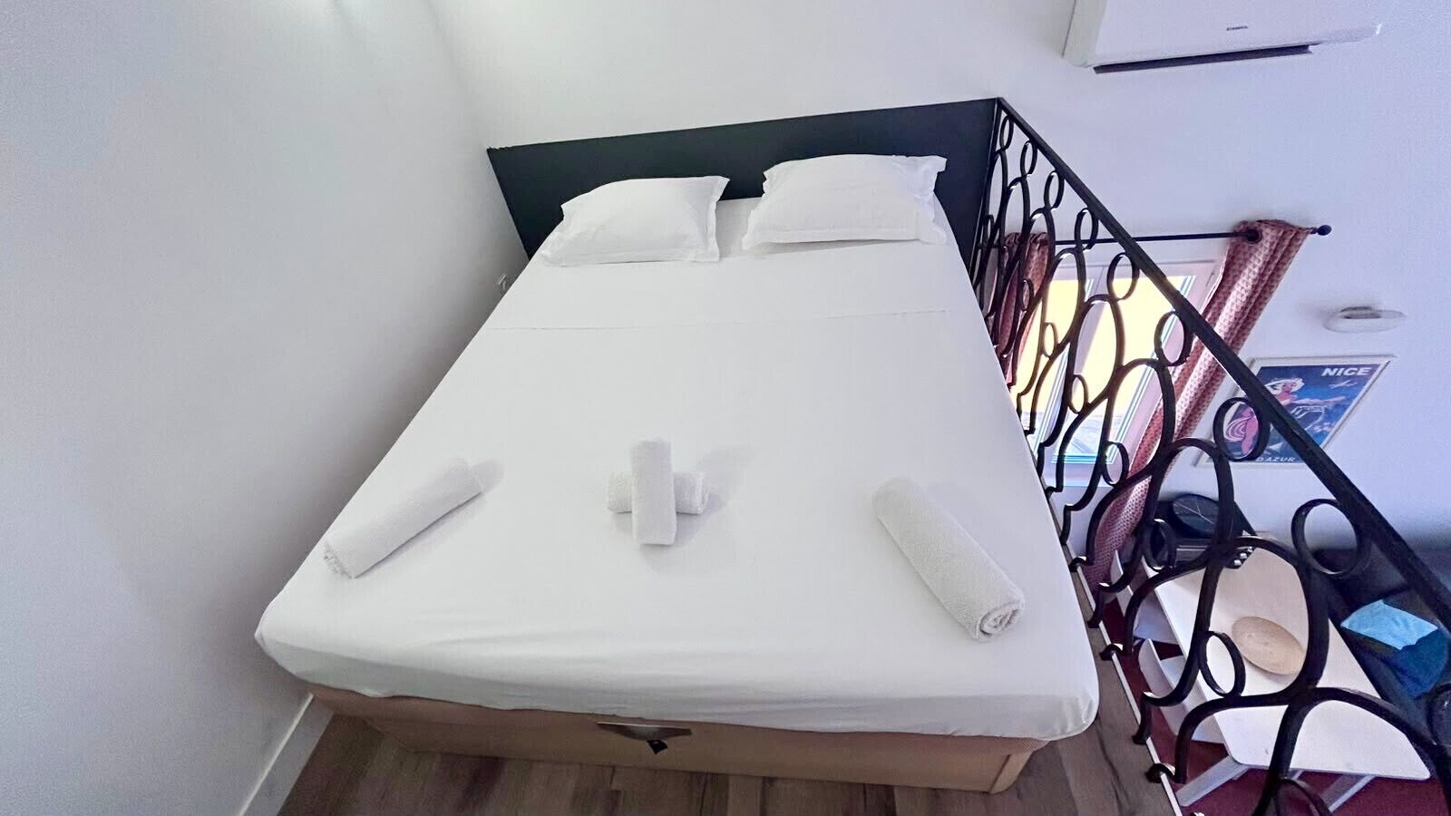 A single bed with white linens and towels, a black metal headboard, and a white wall.