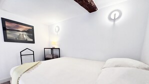 Ein Schlafzimmer mit einem Bett, einem Nachttisch, einer Lampe, einer Wandleuchte und einem gerahmten Bild.